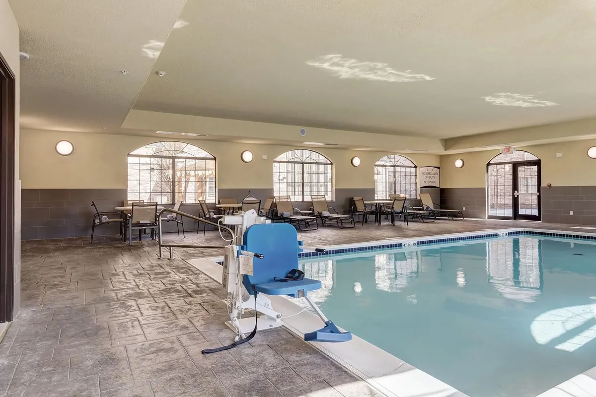 This bright interior image features the indoor swimming pool with lounge chairs, large arched windows letting in natural light, and a pool lift for accessibility. The mood is relaxed and welcoming, perfect for family fun and downtime.