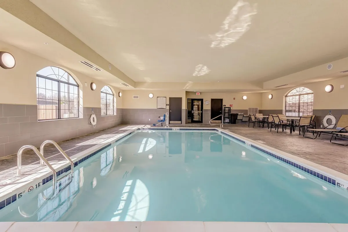 A bright, spacious indoor swimming pool with lounge chairs arranged along large windows that let in plenty of natural light. A lifebuoy is visible on the wall, contributing to a feeling of safety and care. The tranquil setting provides a restful atmosphere ideal for relaxation or gentle exercise.