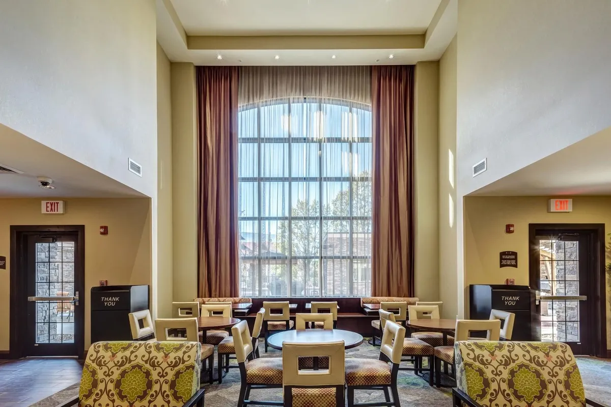 A comfortable social lounge with a large arched window, cozy seating, decorative curtains, and a round table. The space is inviting, ideal for socializing, reading, or relaxing—perfectly capturing the communal, homey feel referenced in the section.