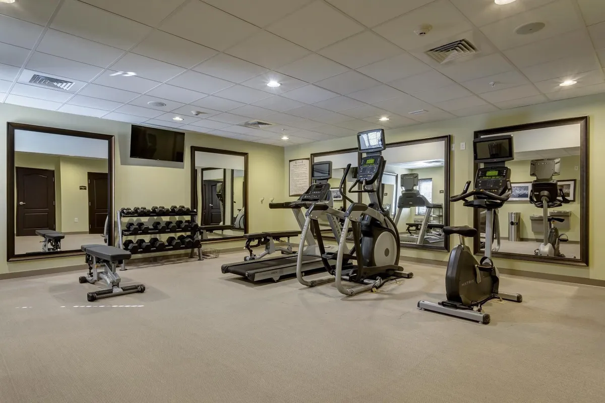 A well-equipped fitness center with a range of exercise machines, free weights, and mirrors. The space has a motivational vibe, ideal for both individual workouts and community fitness activities, emphasizing health and wellness for guests.