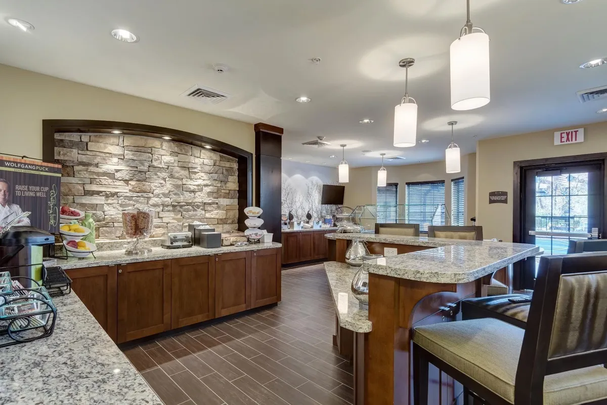 An inviting breakfast area featuring a granite countertop buffet, a striking stone feature wall, and soft pendant lighting. The space is set for guests to enjoy complimentary breakfast, with an atmosphere that feels both welcoming and conducive to starting a productive day.
