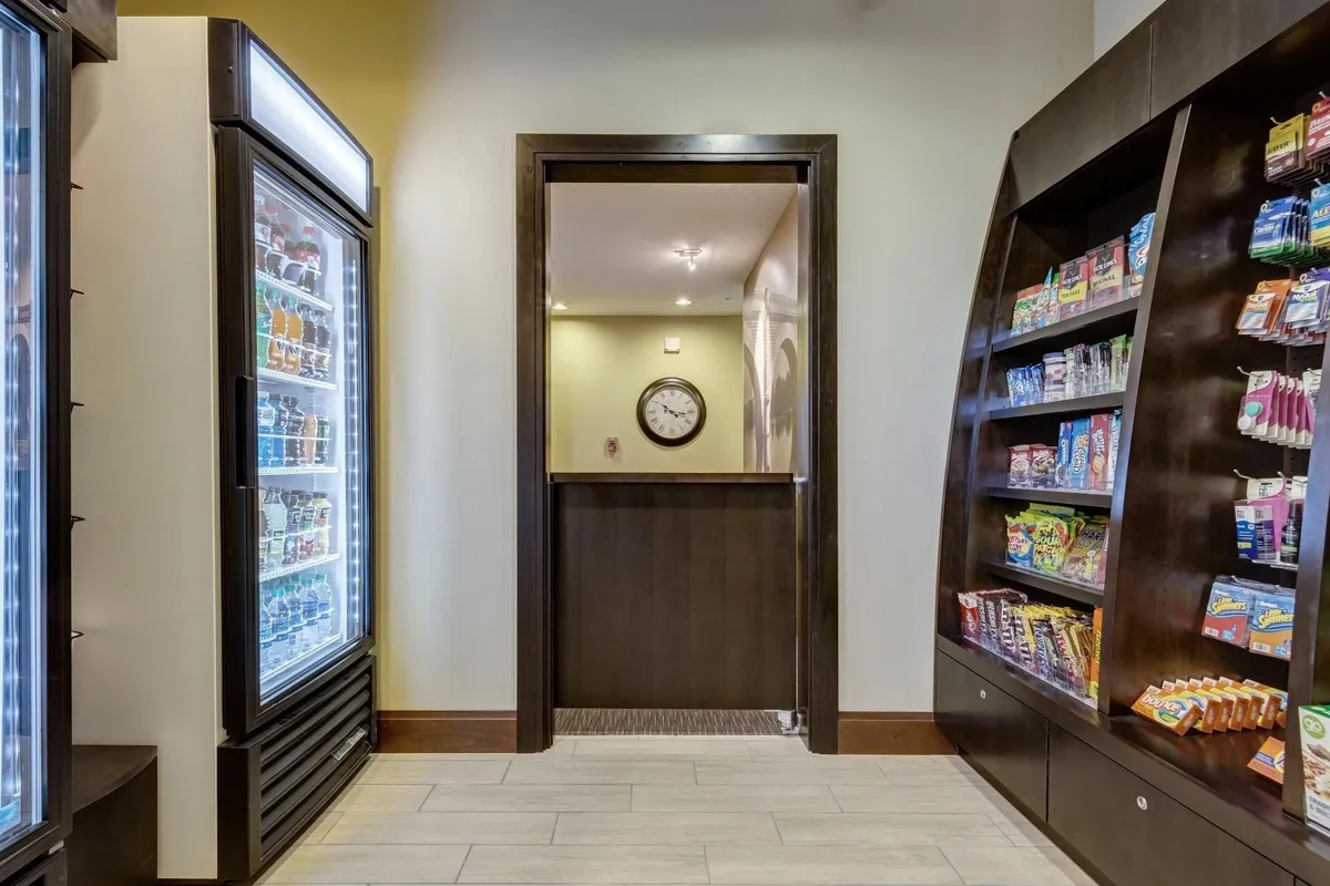A casual refreshment corner featuring a beverage cooler, shelves with snacks, and a wall clock. The setting is inviting for guests seeking a quick bite or a drink, enhancing the sense of convenience and self-sufficiency.