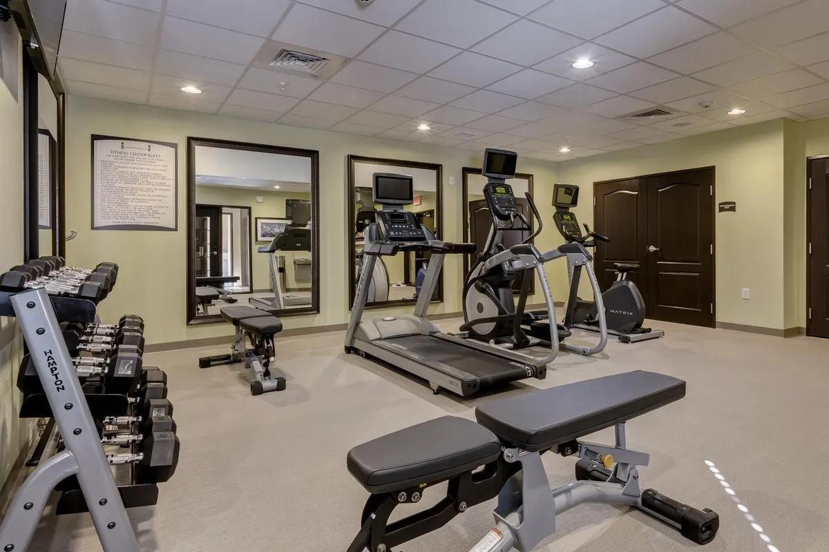 This image depicts a well-equipped fitness center, featuring a treadmill, elliptical machine, dumbbell rack, and weight bench. The space is clean, modern, and inviting, with ample natural light to encourage guests to stay active during their extended stay. The arrangement of equipment suggests a welcoming environment for both serious workouts and casual exercise.