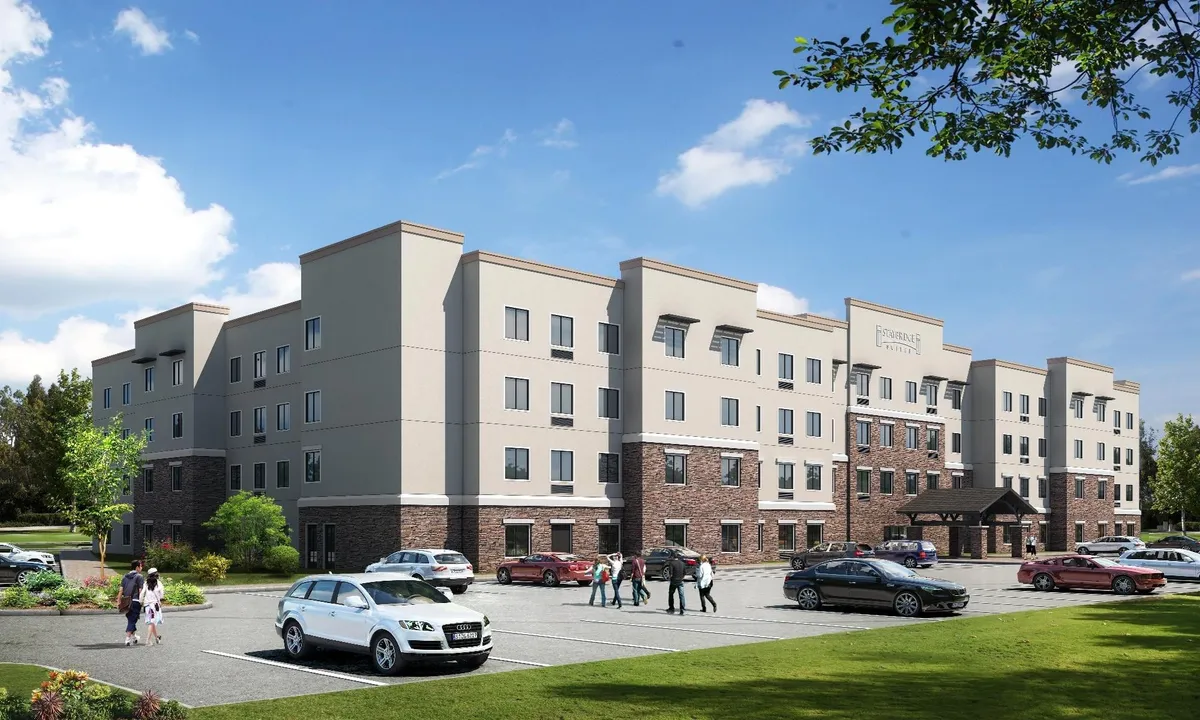 The image showcases the hotel’s exterior, featuring the main building facade, an inviting entrance awning, well-maintained greenery, and families arriving or unloading luggage. The setting conveys a welcoming atmosphere, perfect for the start of a family adventure.