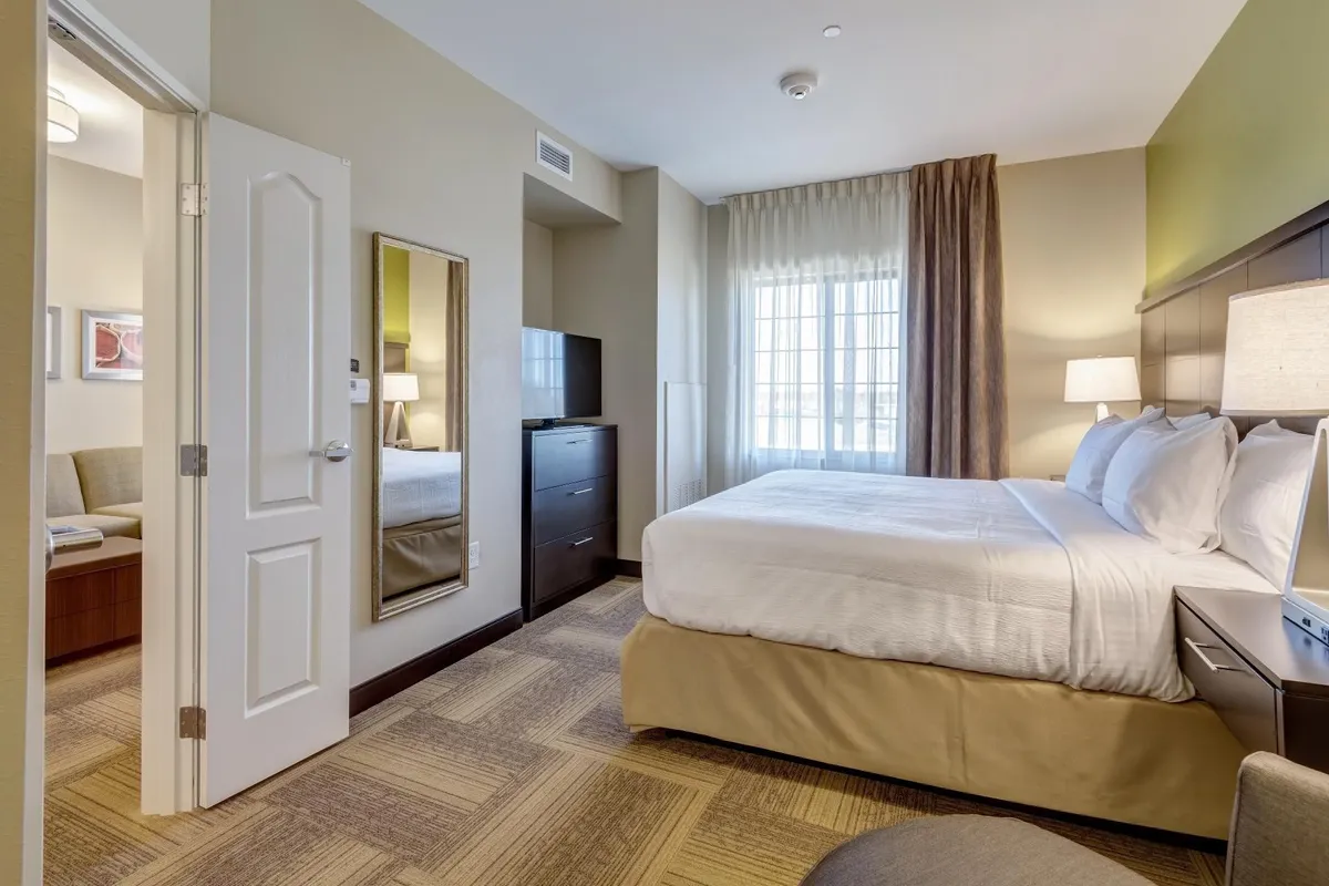 A soothing suite showcasing a plush King bed beside a window streaming with natural light. A cozy sofa and a wall-mounted mirror complete the scene, creating a harmonious space designed for relaxation, reading, or unwinding after a busy day.